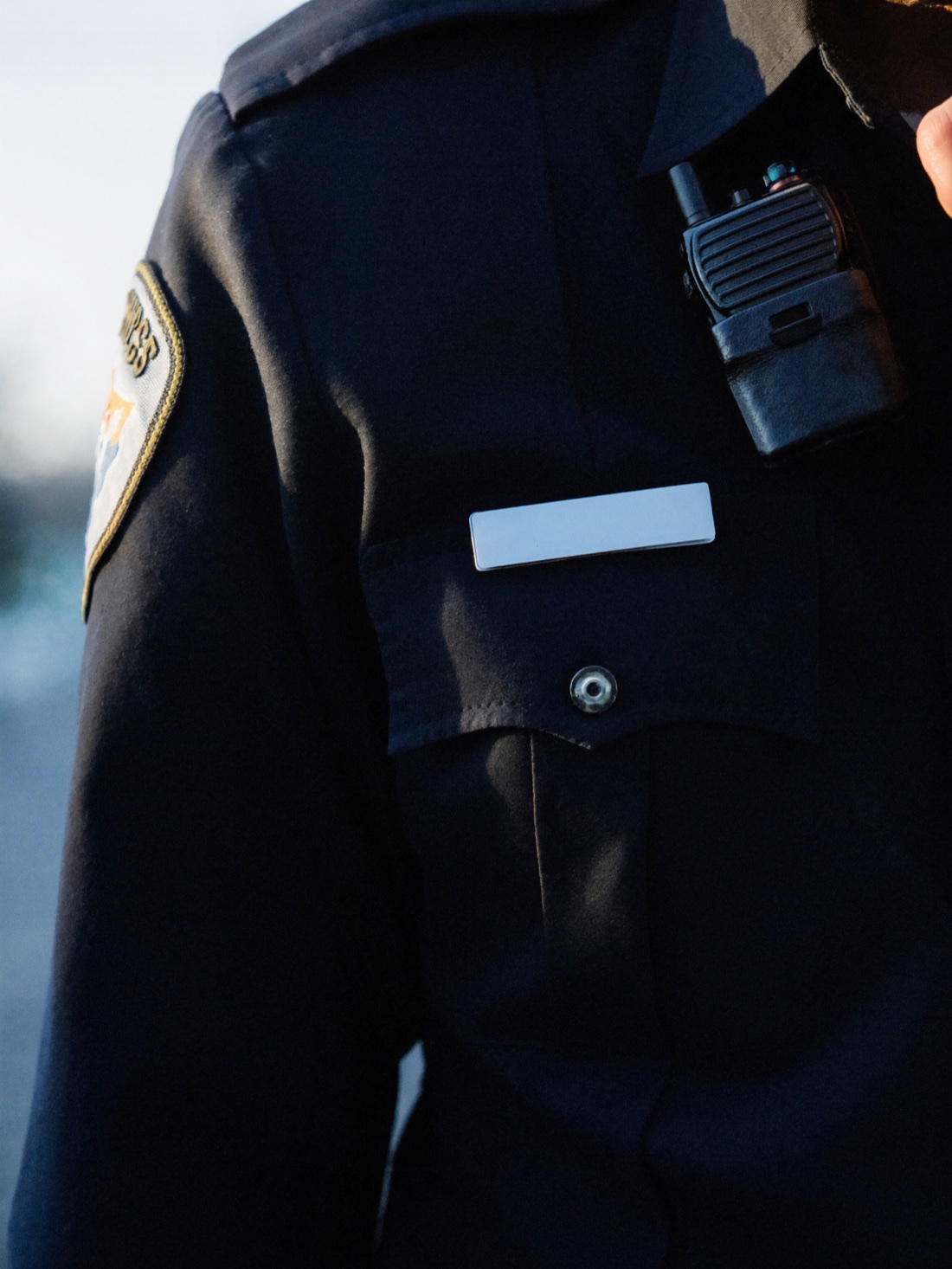 A licensed private security officer's navy uniform with shoulder patch, radio, and name plate